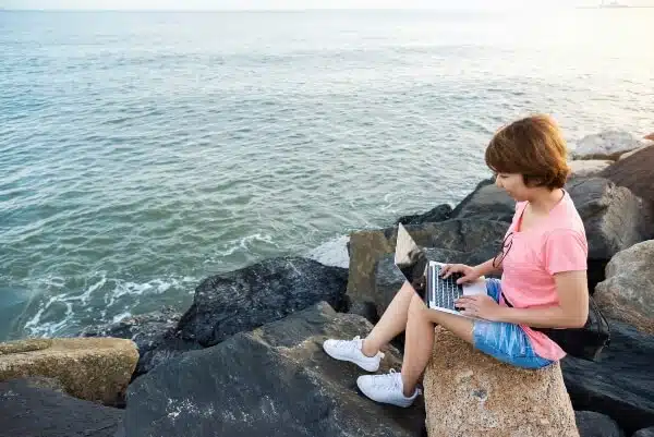 Female travel blogger blogging her first blog post ideas by the coastal sea.