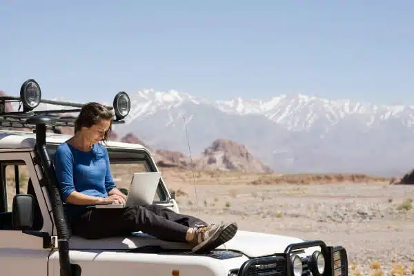 A female blogging sitting on her car and planning her travel blog post ideas.