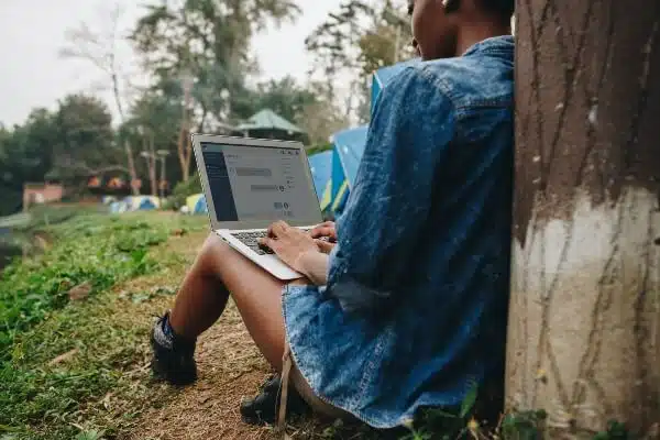 A female blogger sitting against a tree trunk and planning her travel blog post ideas.